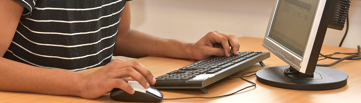 Eine Person arbeitet an einem Computer-Arbeitsplatz mit Tastatur und Maus.