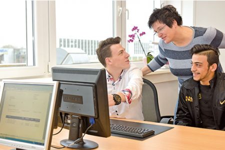 Eine Frau und zwei Männer besprechen Aufgaben an einem Computerarbeitsplatz in einem Büro.