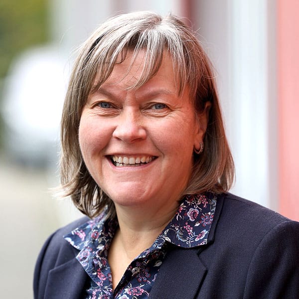 Porträt von Helia Geller-Fehling, lächelnd in dunklem Blazer und gemusterter Bluse.