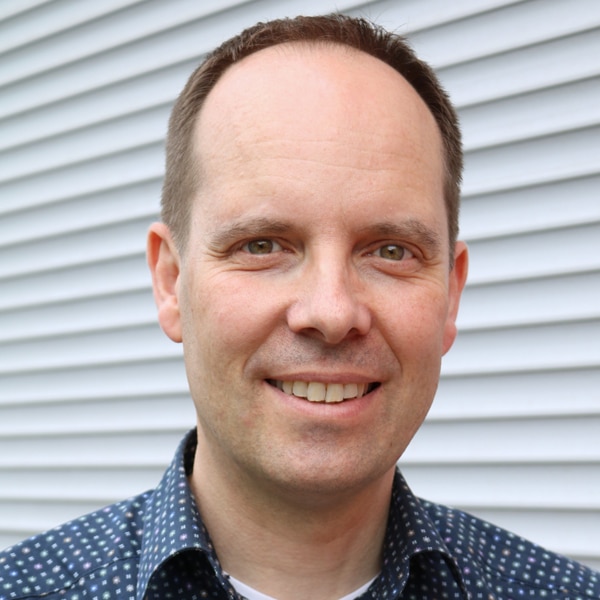 Porträt von Matthias Hohgräbe, ein lächelnder Mann in einem blau gemusterten Hemd.