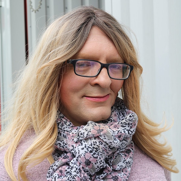 Porträt von Camille mit langen blonden Haaren, einer Brille und einem gemusterten Schal.