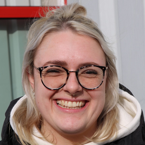 Porträt von Tiffany Schröder, einer lächelnden Frau mit Brille und blonden Haaren.