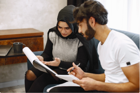 Eine Frau mit Hijab und ein Mann besprechen konzentriert Unterlagen für das Juniver-Projekt.